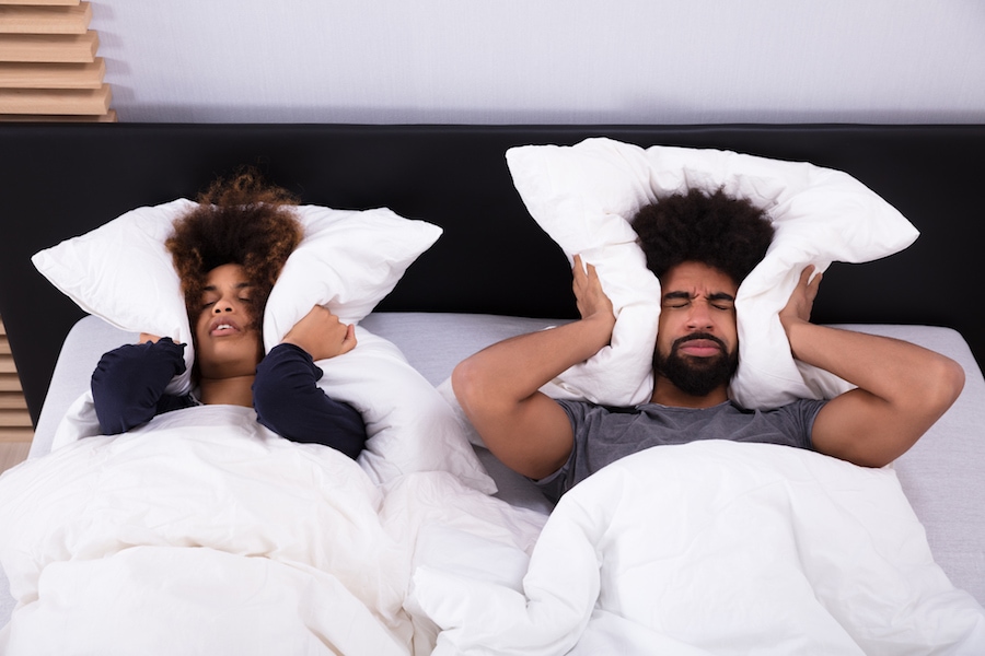 Elevated View Of Young Couple Lying In Bed Covering Their Ears With Pillow.