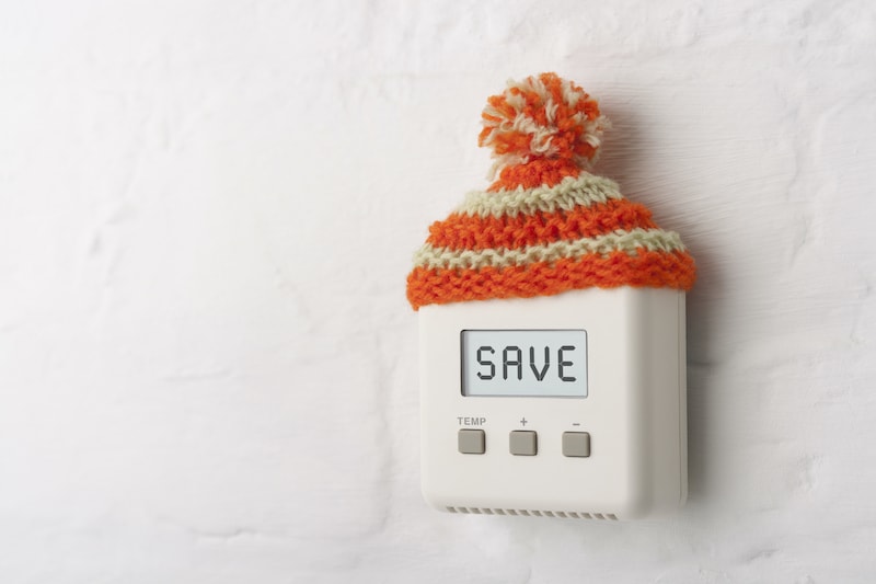 Thermostat with the words SAVE on it, wearing a winter hat.