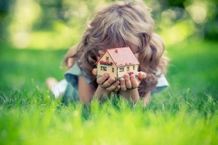 Girl in grass with toy house.