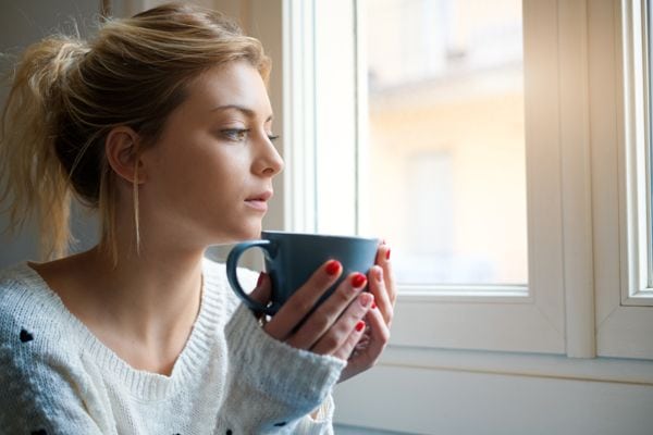 A woman sits next to a window with a coffee cup. Should I Get an 80% or 95% Furnace?