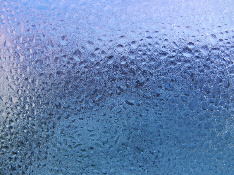 Dark background of the condensate flowing water on the window glass.