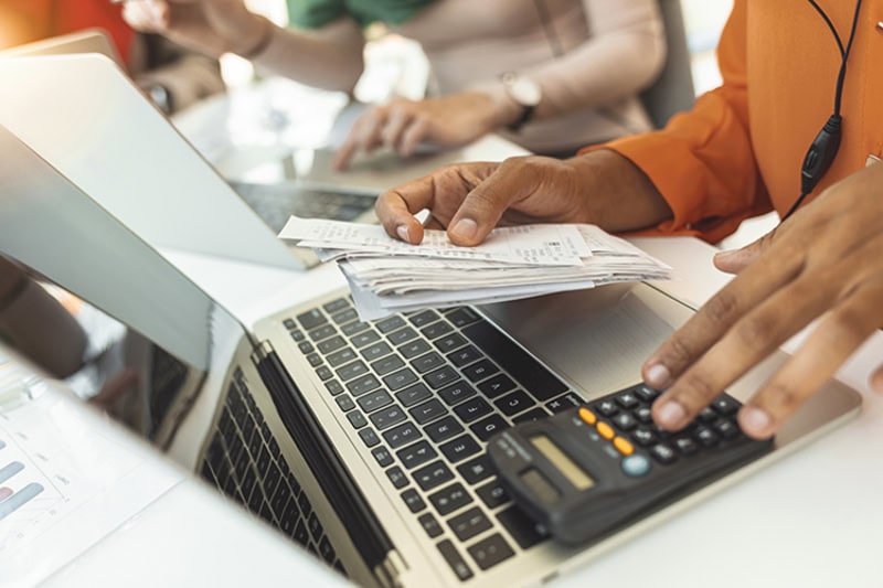 A person looking at bills in front of a laptop.