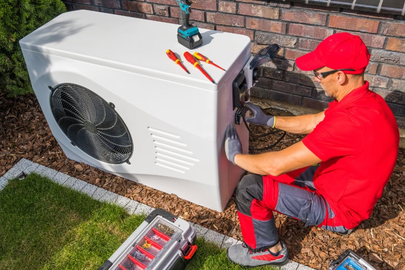 HVAC Technician in Red Uniform Repairing Modern Heat Pump Unit.